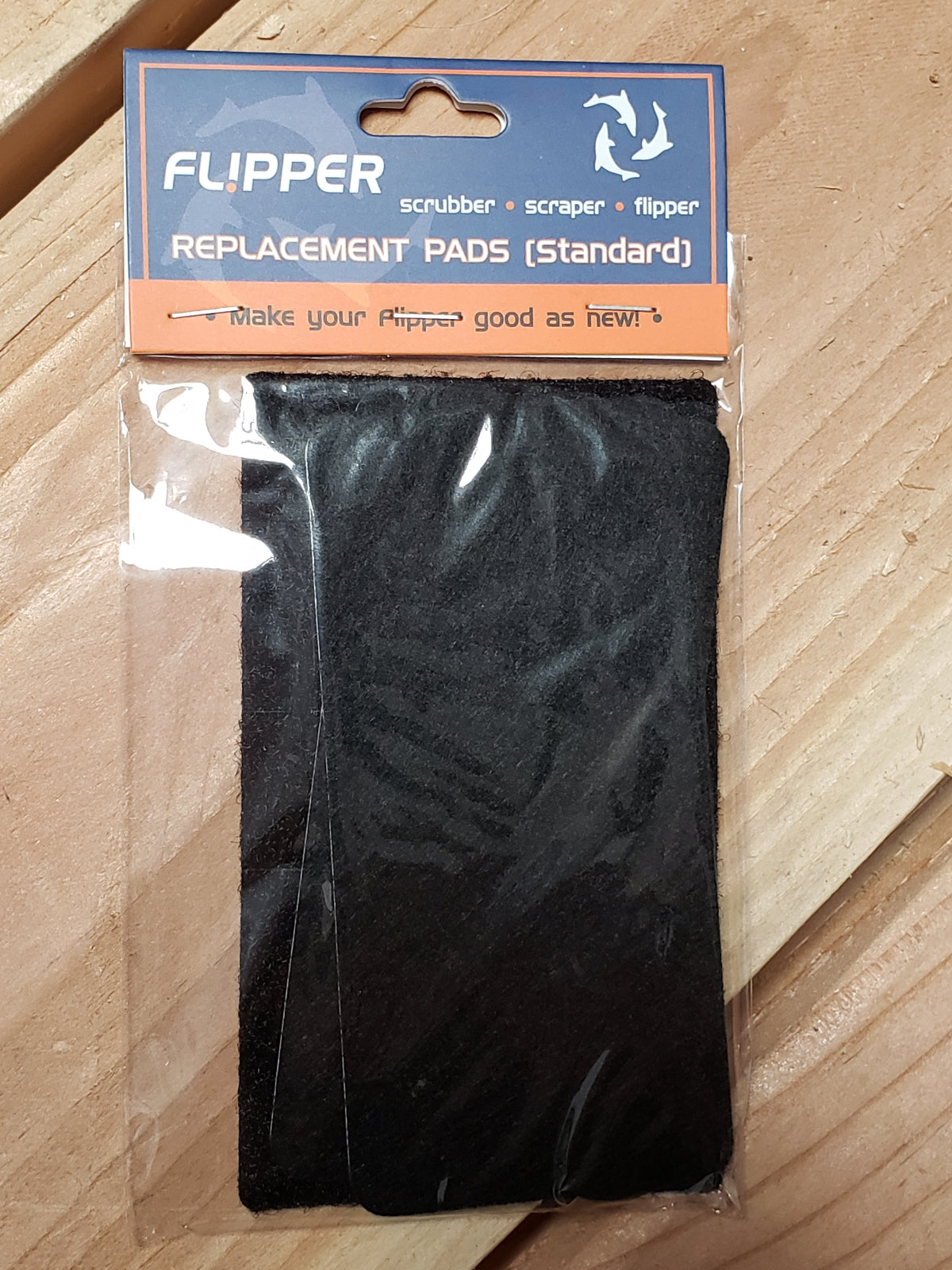 A pair of black replacement pads for the Flipper scrubber, packaged in a clear plastic bag with a orange and white branding label on top.